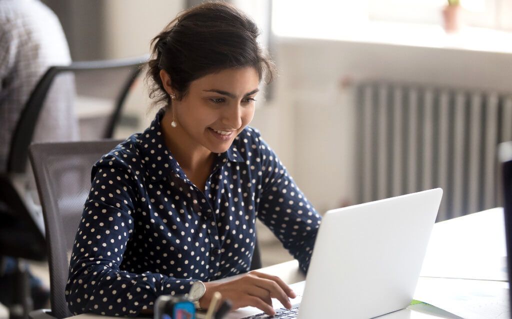 A smiling woman looking at her laptop screen