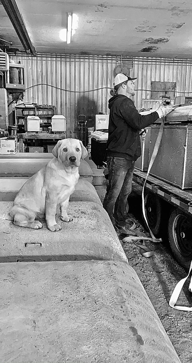 Tyler and Jameson in the shop where Tyler is securing a vault to a trailer for delivery 