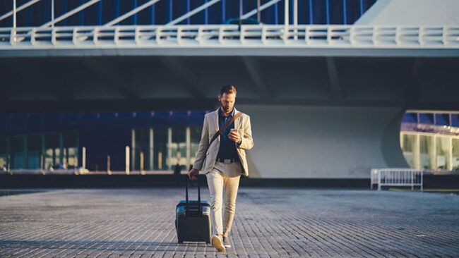 Young businessman with suitcase just arriving in Valencia and texting on phone