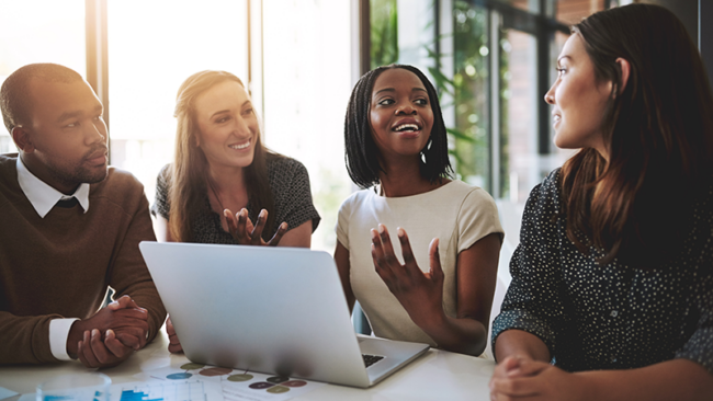 group of people smiling at each other sitting in an office in front of a computer talking