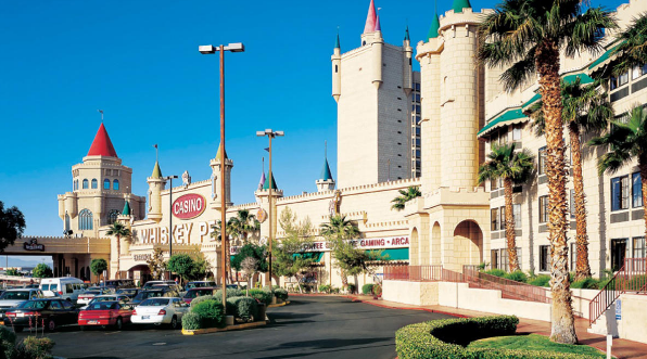 Outside of Whiskey Pete's Casino. The casino is shaped like a castle, with clear blue skies and the parking lot filled with cars.