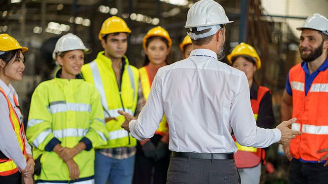 manager talking to a crew with safety vests and hard hats on